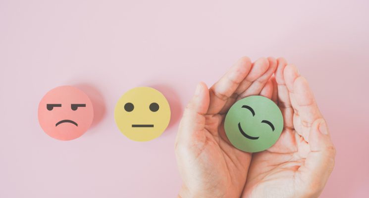 hand holding green paper cut happy smiling face on pink background for mental health assessment ,positive thinking, world mental health day ,customer review, experience, satisfaction survey concept